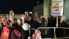 DemonstrantInnen mit Megafon hinter Absperrgitter